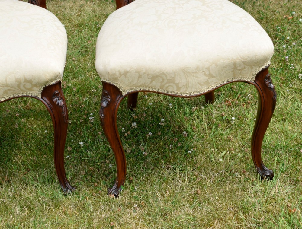 A set of four Victorian walnut dining chairs featuring carved balloon backs, cream upholstered seats, and curved cabriole legs. View XV