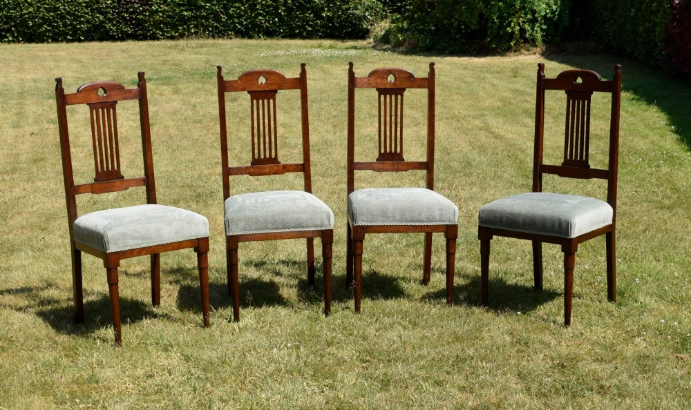 A set of four dark oak Arts and Crafts dining chairs with heart cutouts on the backrests and light grey upholstered seats. View IV