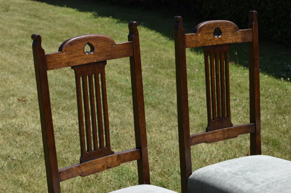 A set of four dark oak Arts and Crafts dining chairs with heart cutouts on the backrests and light grey upholstered seats. View VI