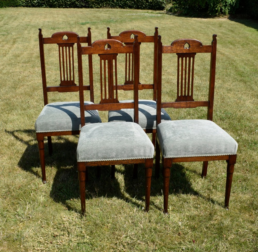 A set of four dark oak Arts and Crafts dining chairs with heart cutouts on the backrests and light grey upholstered seats. View IX