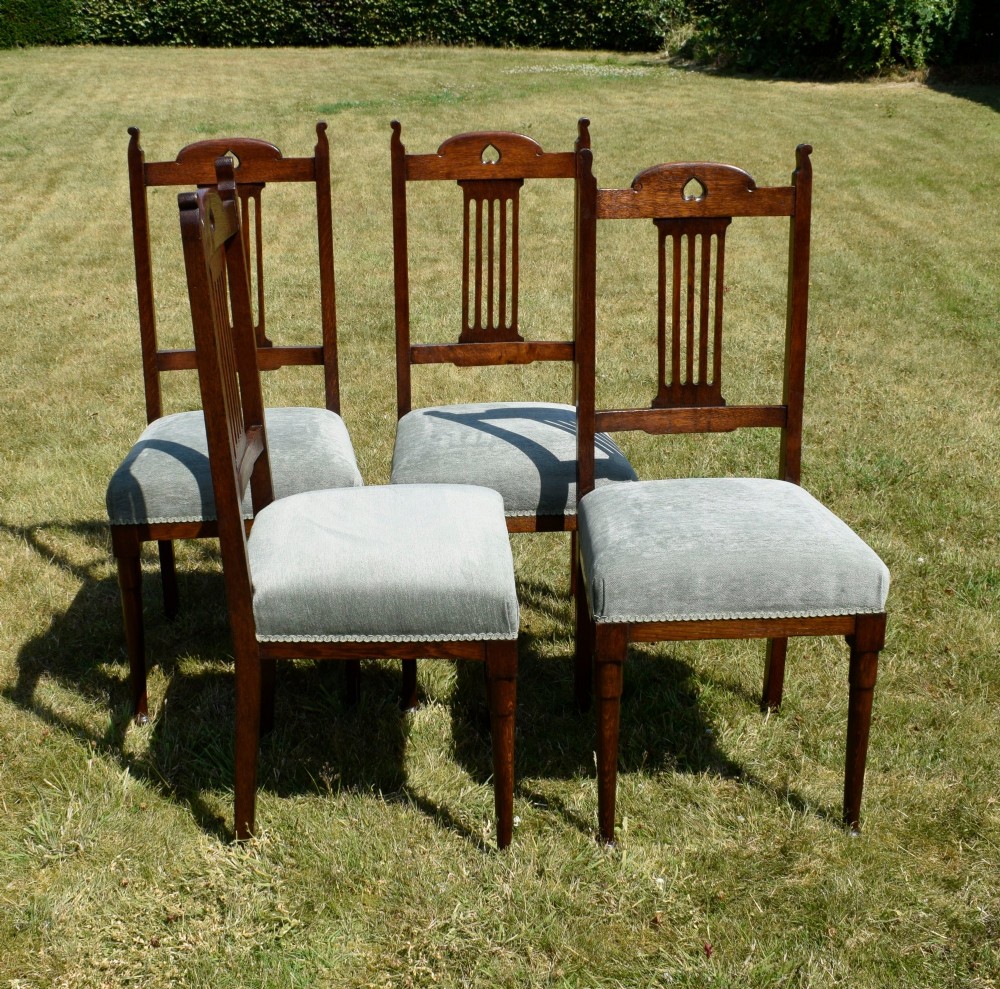 A set of four dark oak Arts and Crafts dining chairs with heart cutouts on the backrests and light grey upholstered seats. View X
