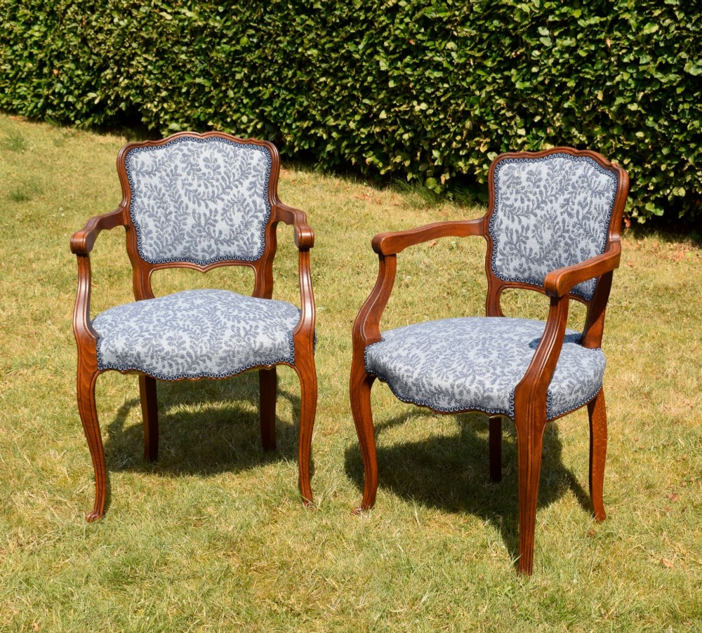 A pair of early 20th-century French armchairs with carved walnut frames, cabriole legs, swept arms, and blue leaf-patterned fabric upholstery.