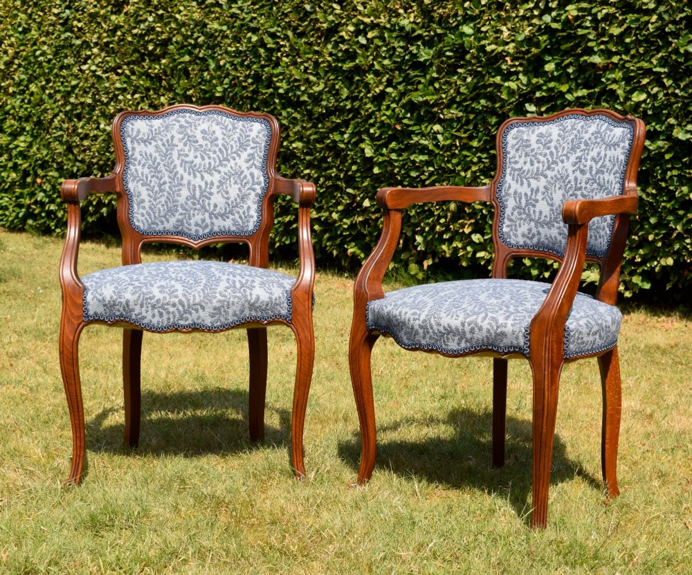 A pair of early 20th-century French armchairs with carved walnut frames, cabriole legs, swept arms, and blue leaf-patterned fabric upholstery. View II