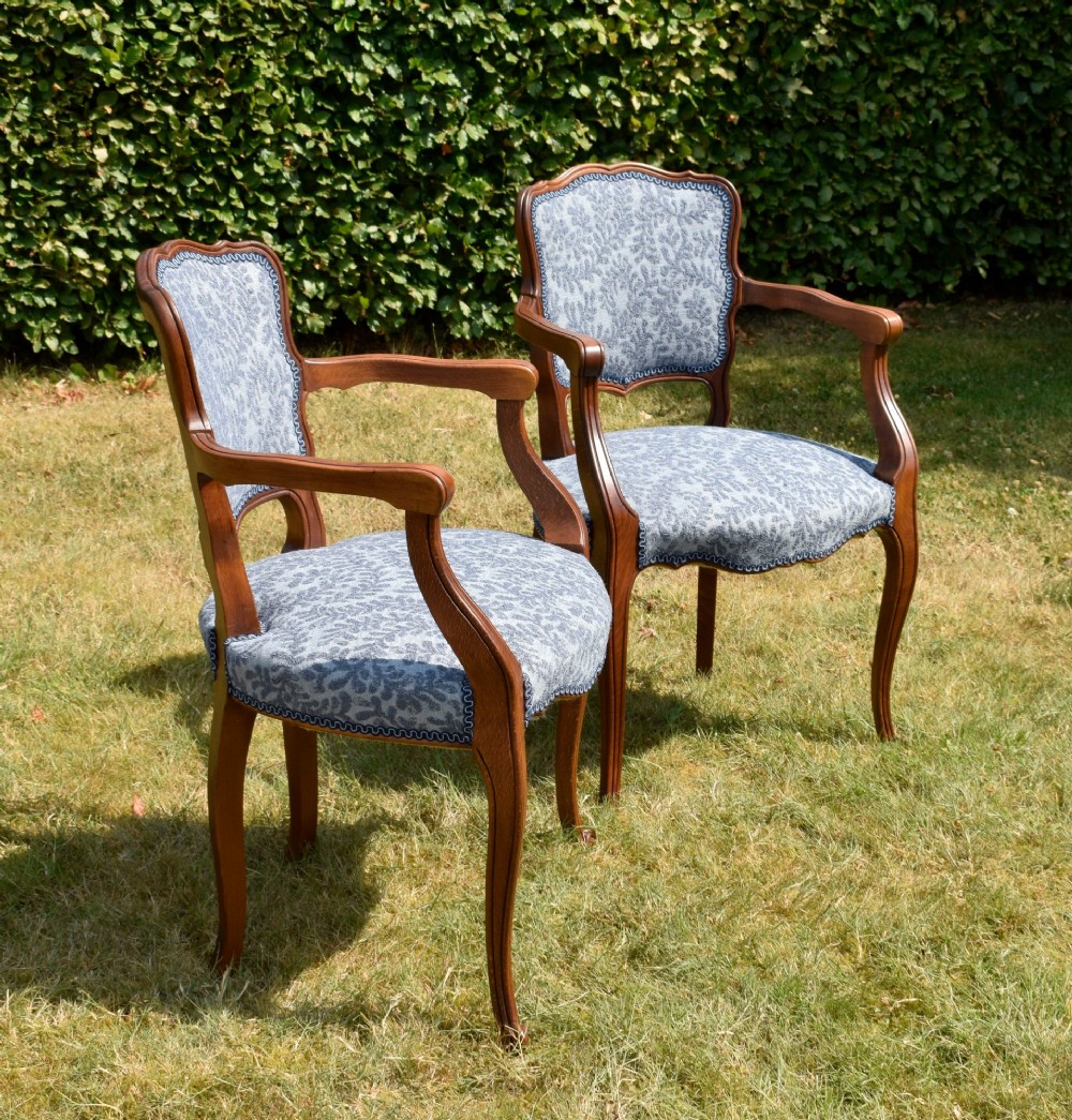 A pair of early 20th-century French armchairs with carved walnut frames, cabriole legs, swept arms, and blue leaf-patterned fabric upholstery. View V