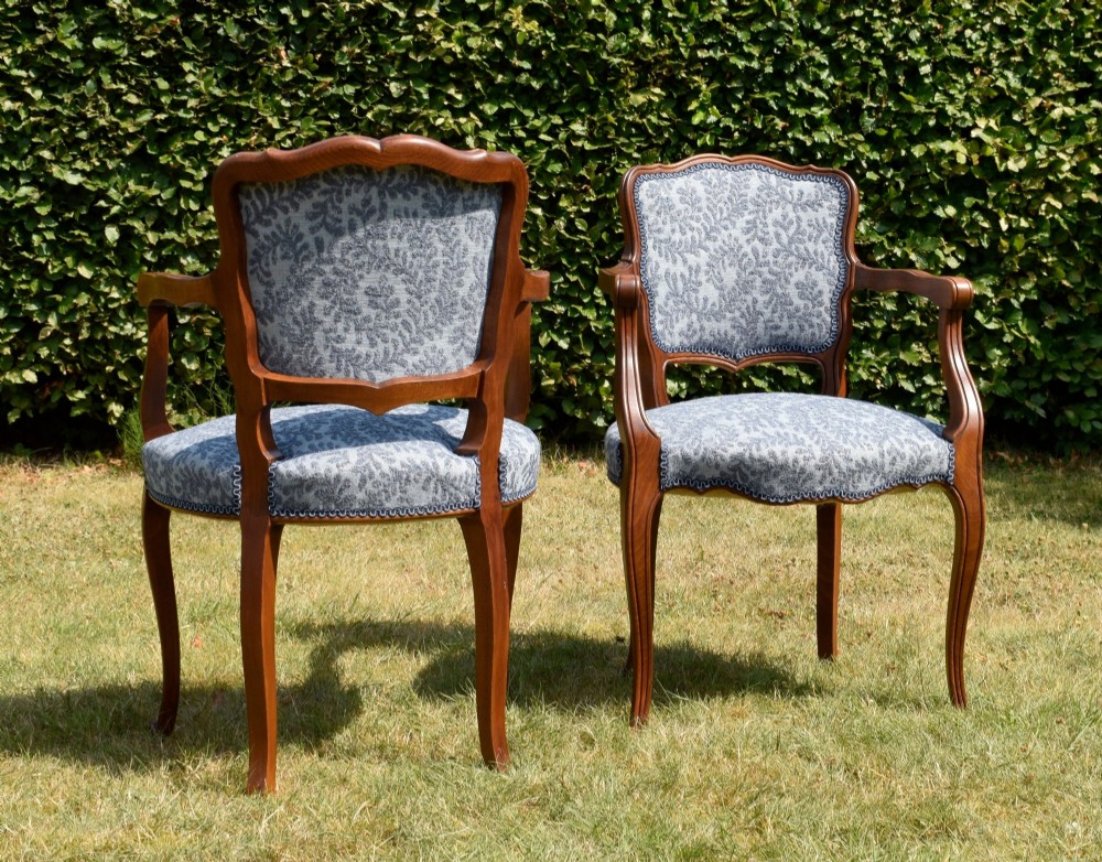 A pair of early 20th-century French armchairs with carved walnut frames, cabriole legs, swept arms, and blue leaf-patterned fabric upholstery. View VI