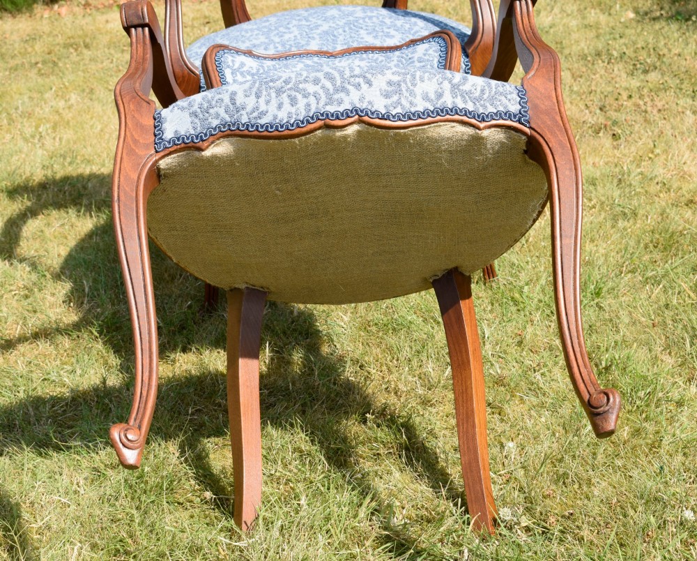 A pair of early 20th-century French armchairs with carved walnut frames, cabriole legs, swept arms, and blue leaf-patterned fabric upholstery. View X