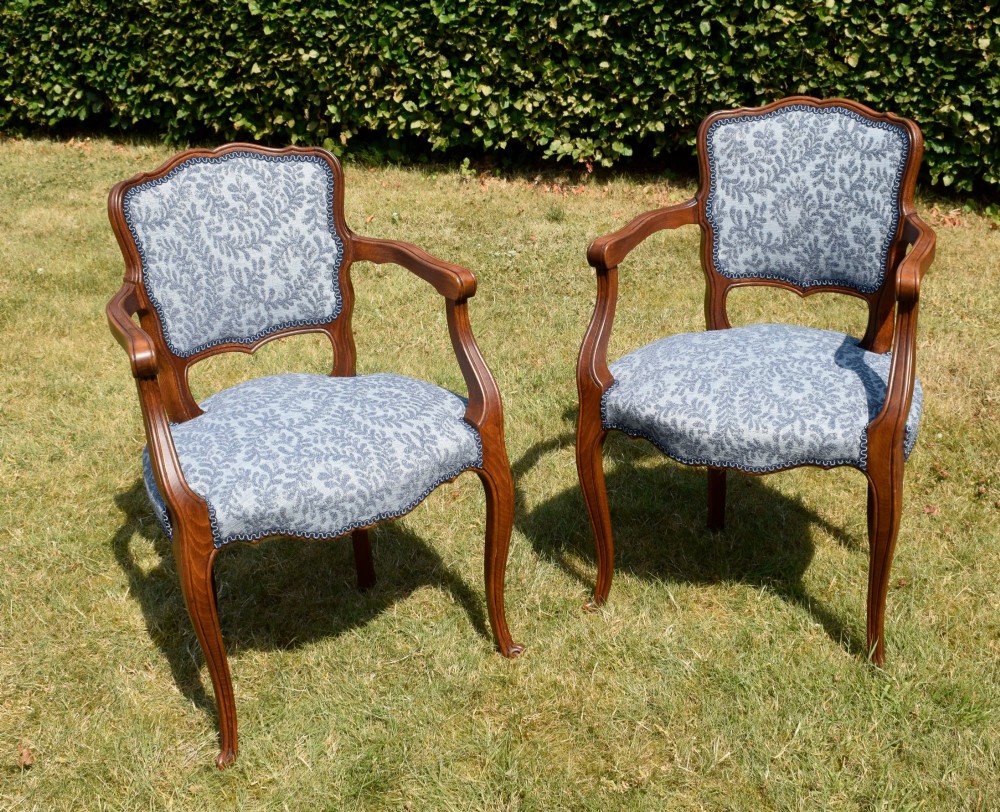 A pair of early 20th-century French armchairs with carved walnut frames, cabriole legs, swept arms, and blue leaf-patterned fabric upholstery. View XIV