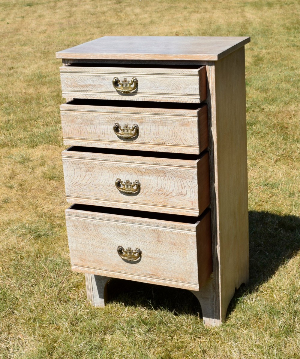A tall Edwardian limed oak chest of drawers with four graduated drawers, brass handles, and a shaped apron base. View IV