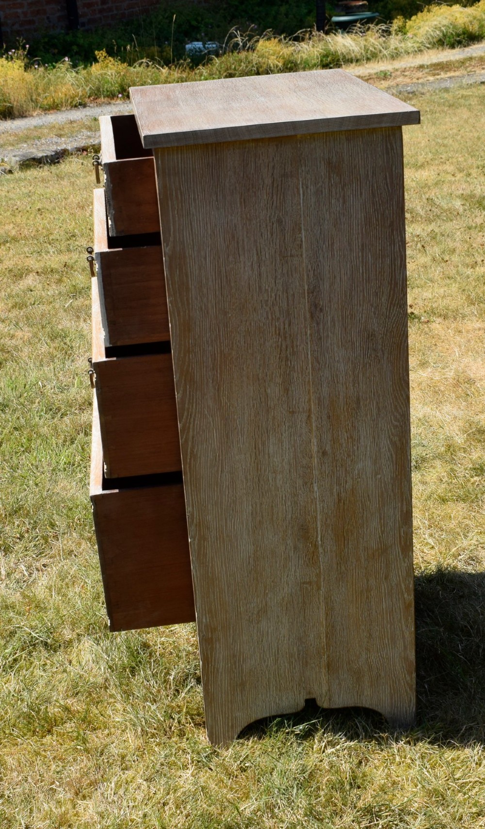 A tall Edwardian limed oak chest of drawers with four graduated drawers, brass handles, and a shaped apron base. View V