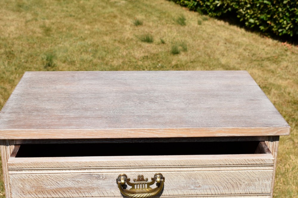 A tall Edwardian limed oak chest of drawers with four graduated drawers, brass handles, and a shaped apron base. View X