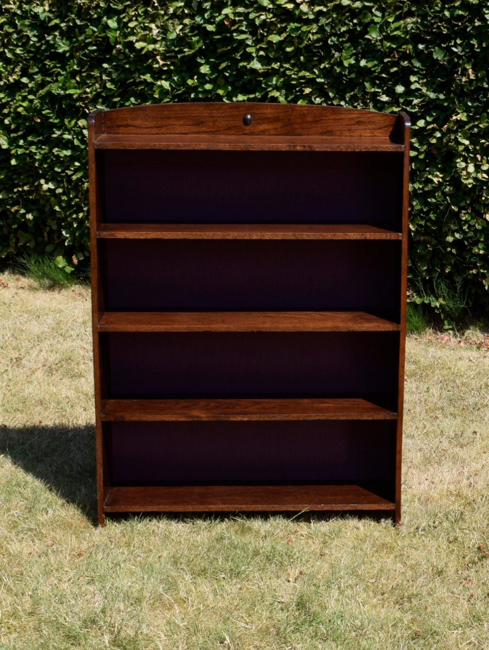 An Arts and Crafts solid oak open bookcase featuring five shelves, solid plank sides, an arched gallery top with a central decorative motif, and a purple fabric-lined back panel. View III
