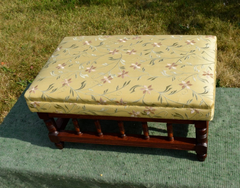 A low rectangular mahogany footstool featuring turned wood spindles and a yellow floral pattern padded fabric top.