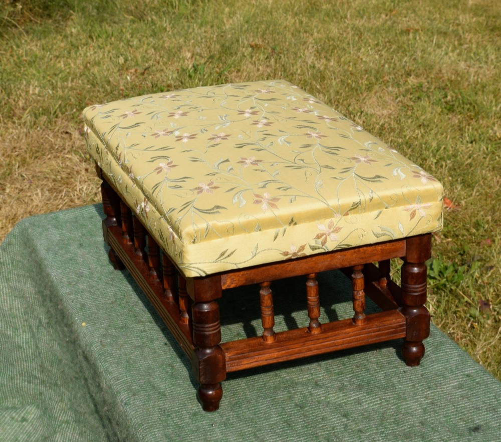 A low rectangular mahogany footstool featuring turned wood spindles and a yellow floral pattern padded fabric top. View II