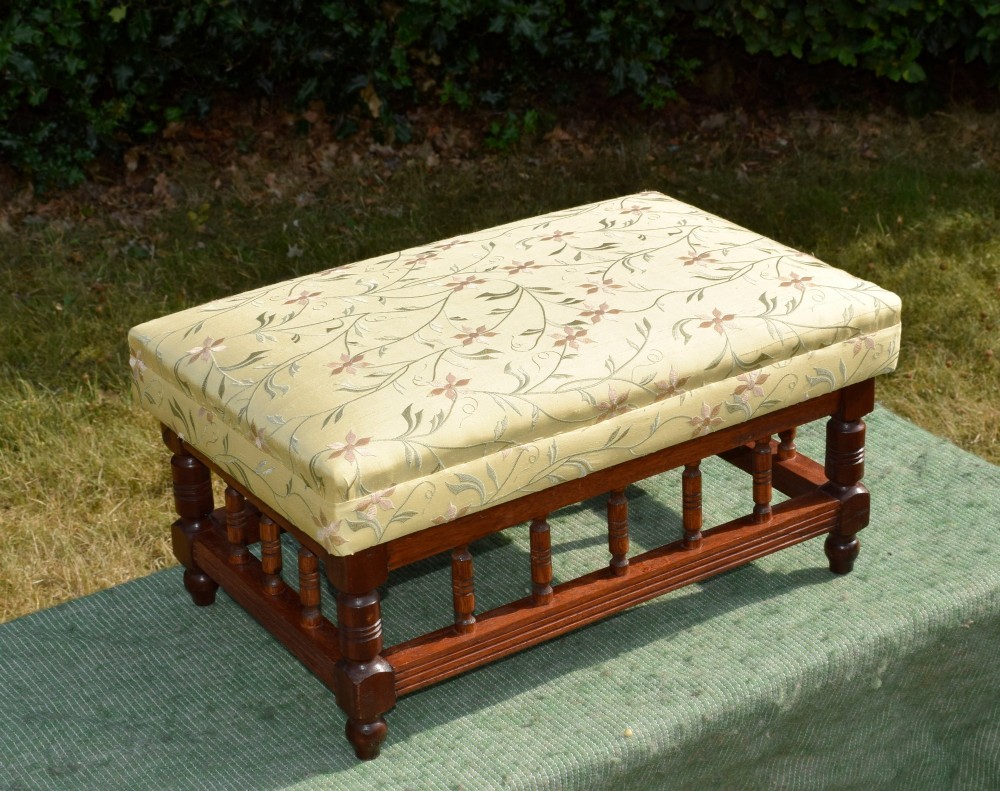 A low rectangular mahogany footstool featuring turned wood spindles and a yellow floral pattern padded fabric top. View IV