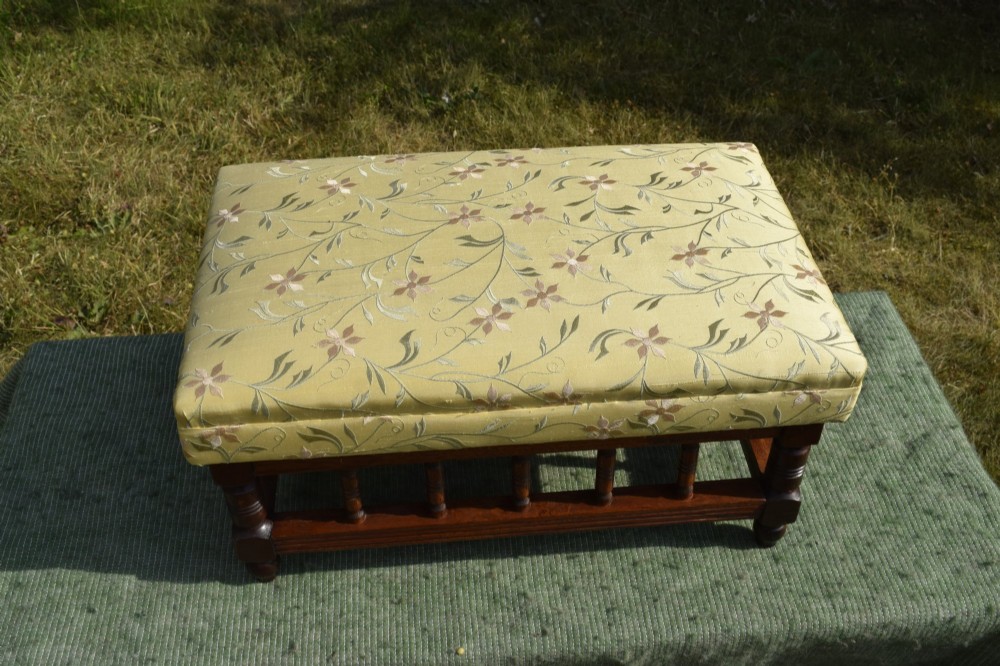 A low rectangular mahogany footstool featuring turned wood spindles and a yellow floral pattern padded fabric top. View V