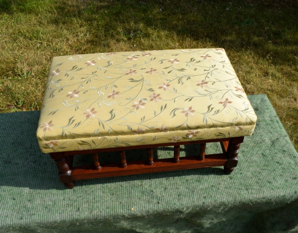 A low rectangular mahogany footstool featuring turned wood spindles and a yellow floral pattern padded fabric top. View VII
