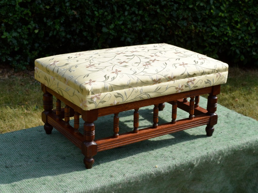 A low rectangular mahogany footstool featuring turned wood spindles and a yellow floral pattern padded fabric top. View X