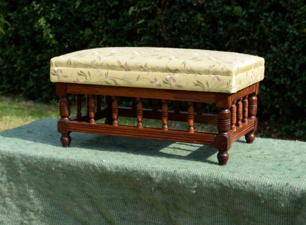 A low rectangular mahogany footstool featuring turned wood spindles and a yellow floral pattern padded fabric top. View XI