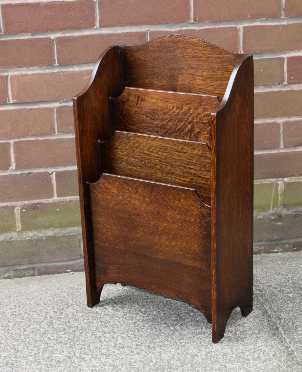 A dark oak Arts and Crafts freestanding magazine rack featuring a gently arched crest rail and three tiered open compartments. View II