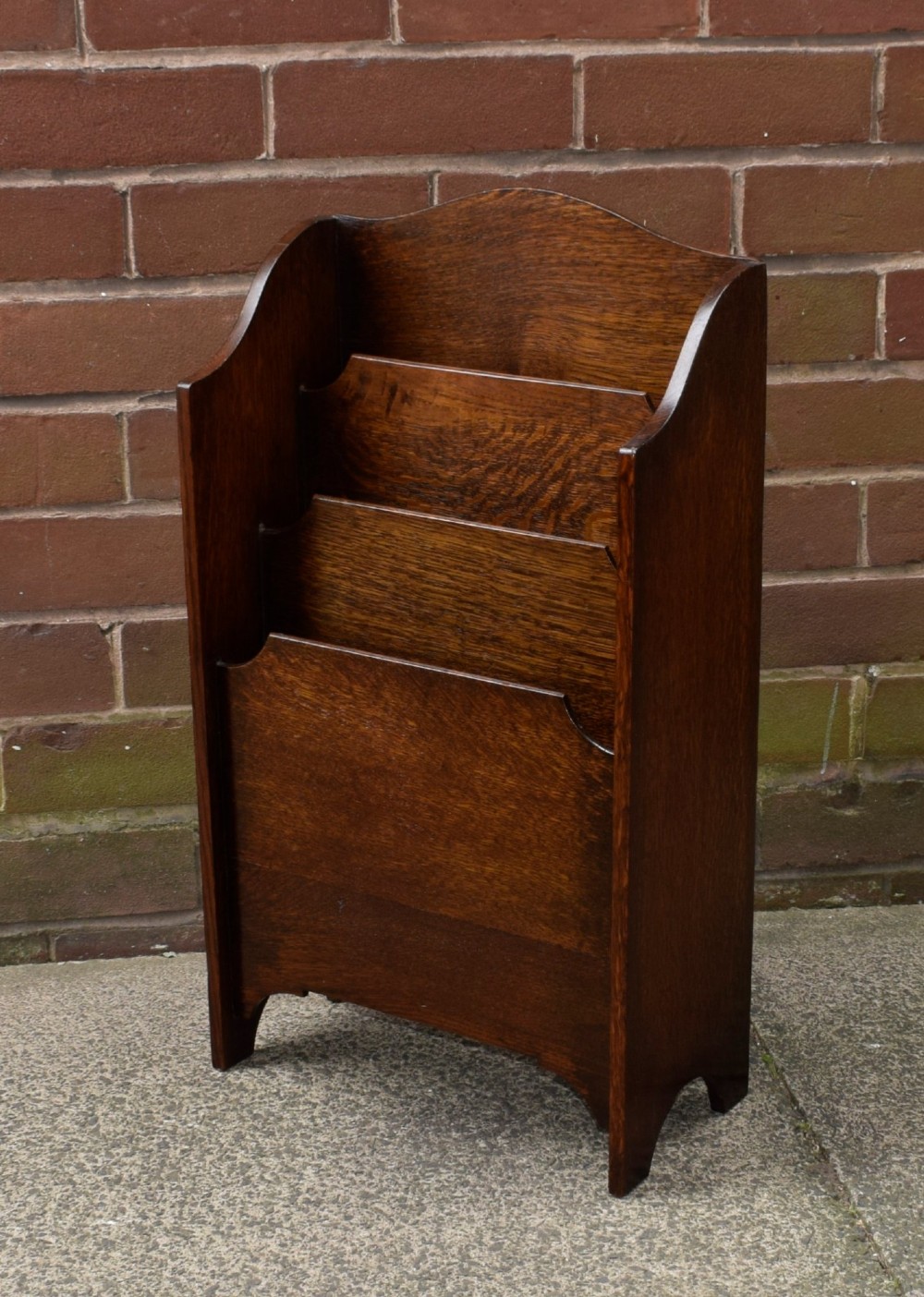 A dark oak Arts and Crafts freestanding magazine rack featuring a gently arched crest rail and three tiered open compartments. View III