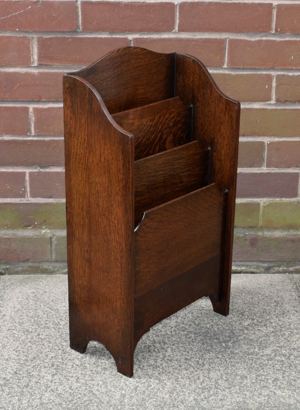 A dark oak Arts and Crafts freestanding magazine rack featuring a gently arched crest rail and three tiered open compartments. View IV