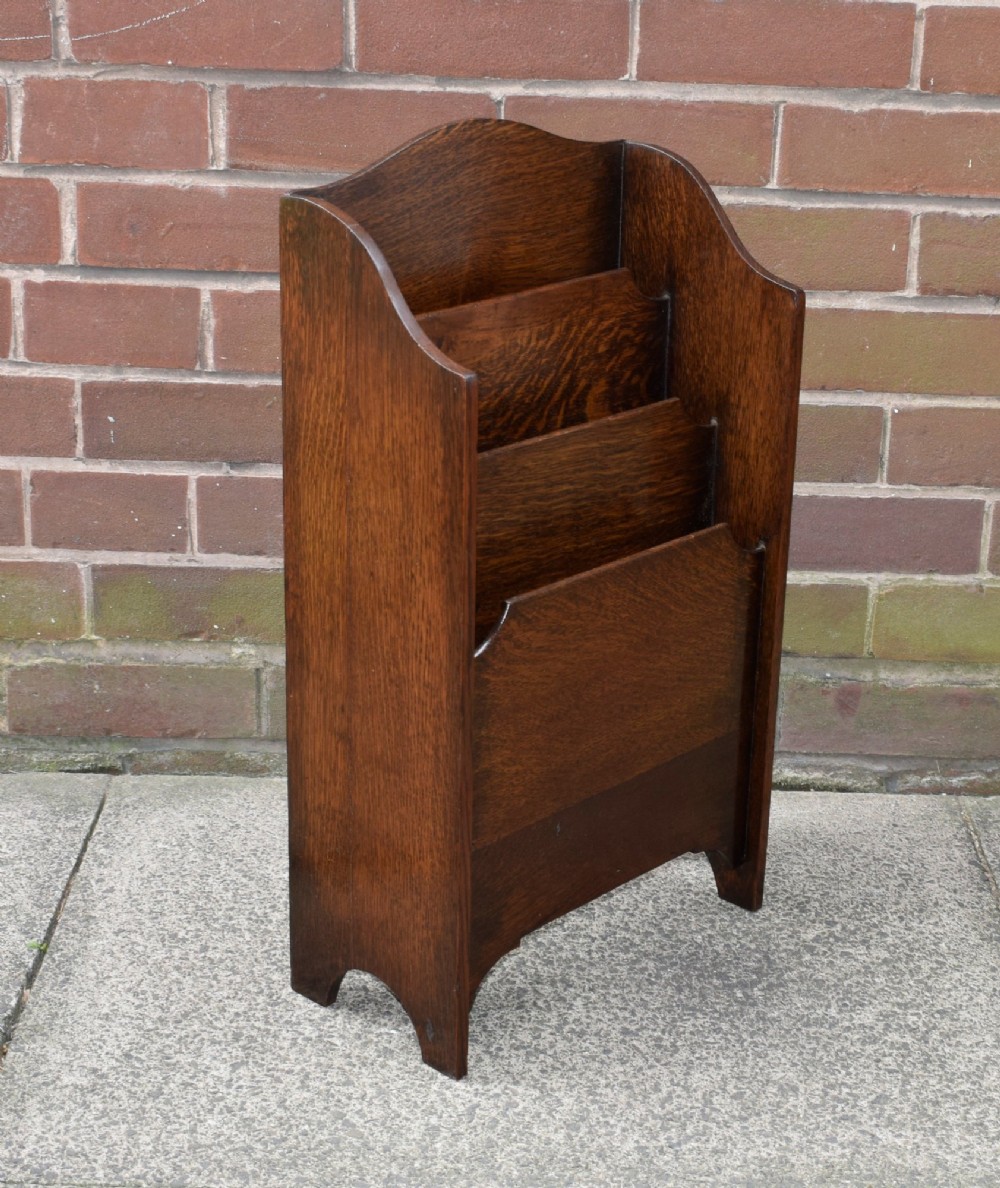 A dark oak Arts and Crafts freestanding magazine rack featuring a gently arched crest rail and three tiered open compartments. View V