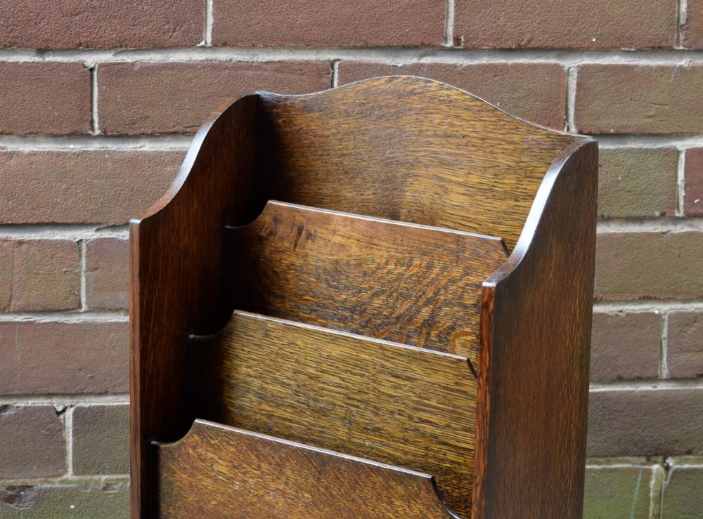 A dark oak Arts and Crafts freestanding magazine rack featuring a gently arched crest rail and three tiered open compartments. View VI