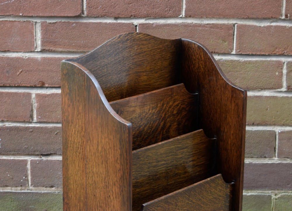 A dark oak Arts and Crafts freestanding magazine rack featuring a gently arched crest rail and three tiered open compartments. View VII