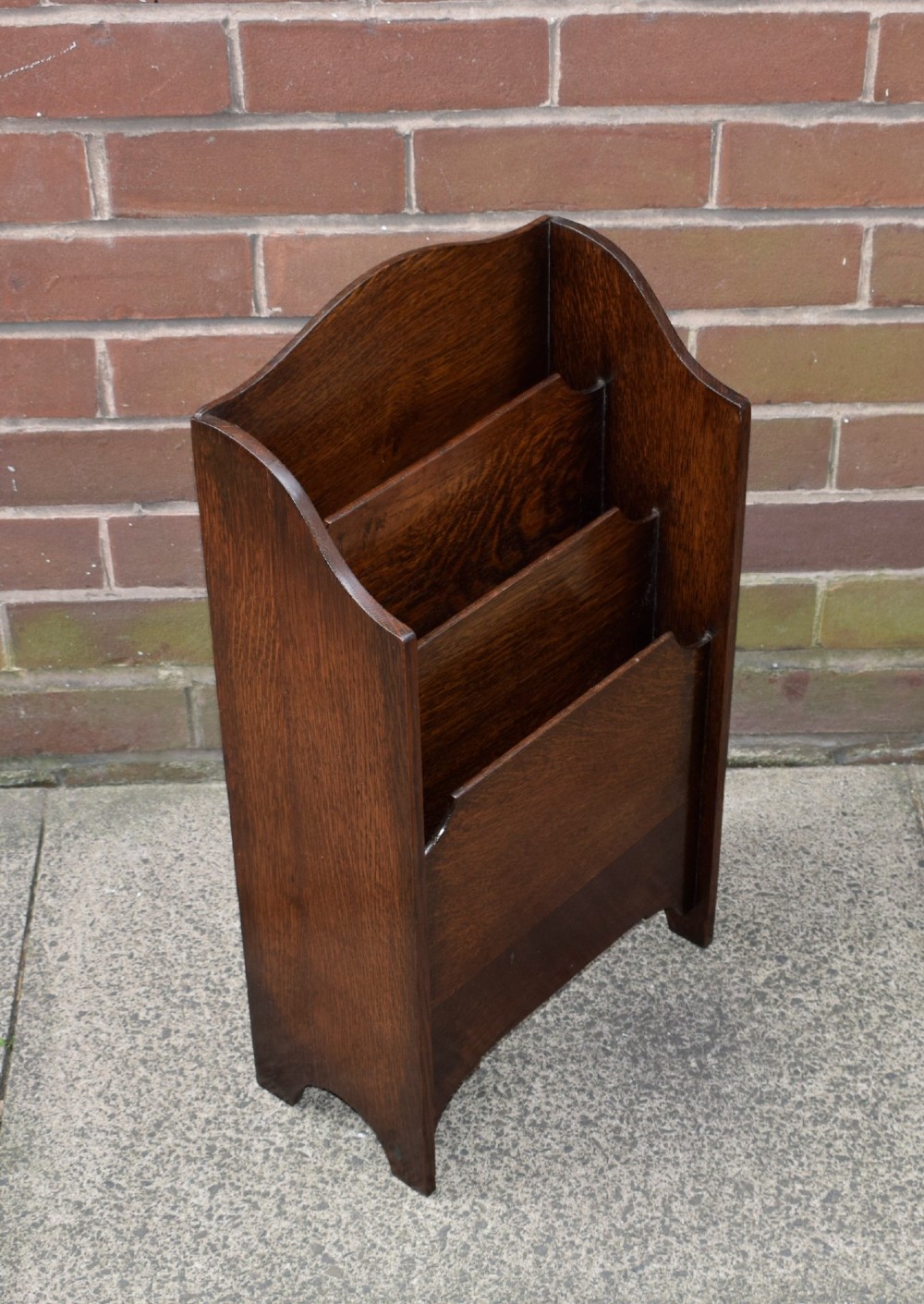 A dark oak Arts and Crafts freestanding magazine rack featuring a gently arched crest rail and three tiered open compartments. View VIII