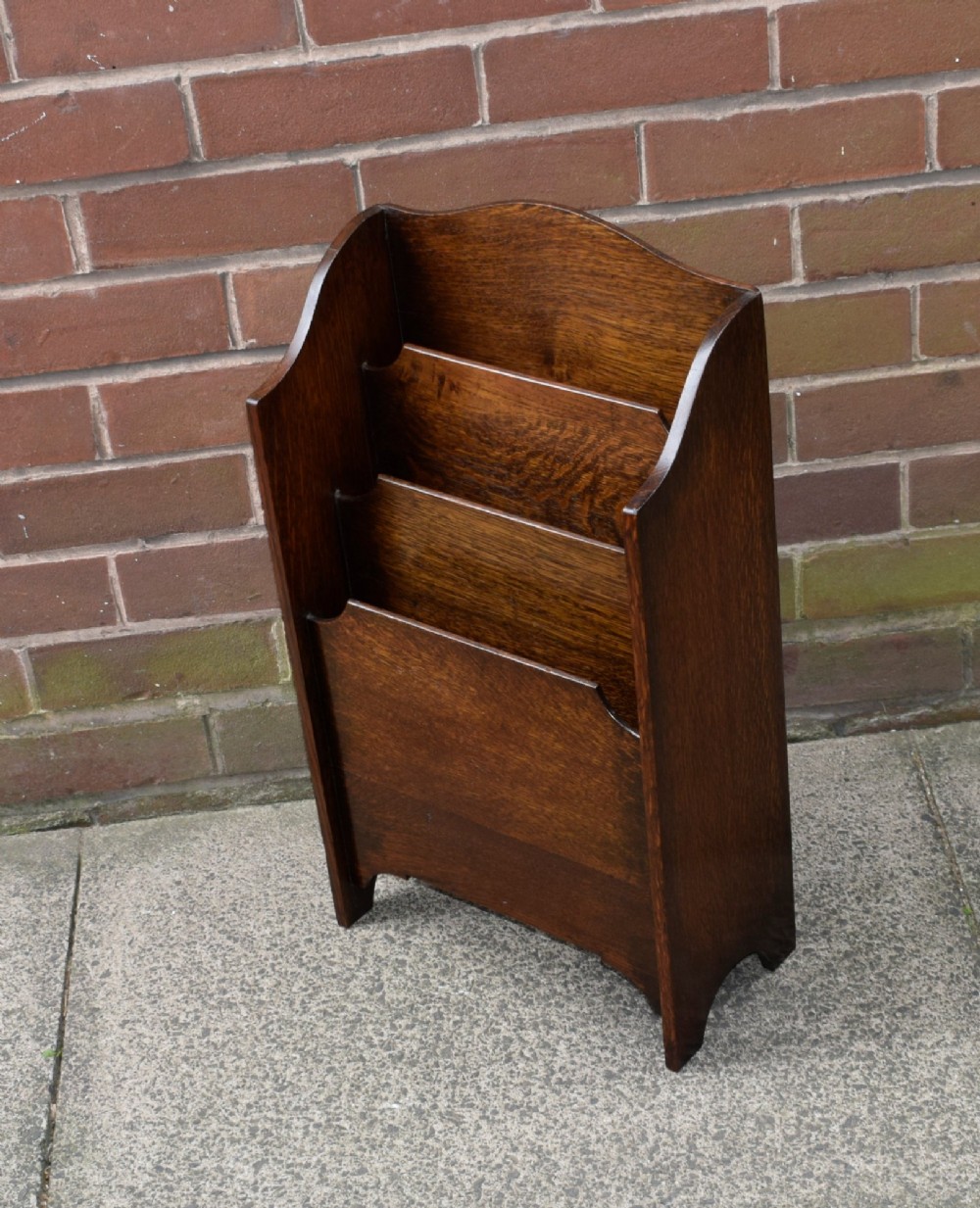 A dark oak Arts and Crafts freestanding magazine rack featuring a gently arched crest rail and three tiered open compartments. View IX