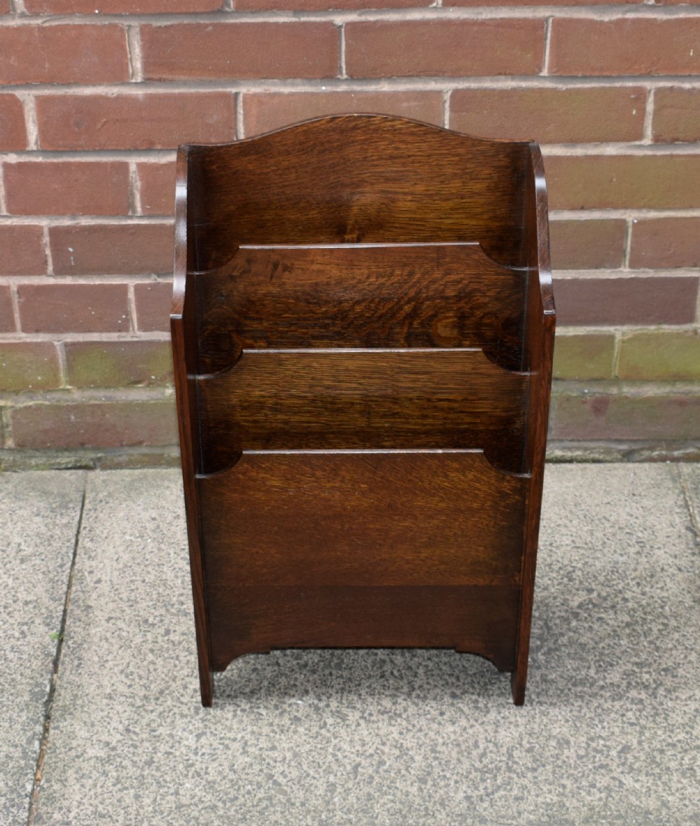 A dark oak Arts and Crafts freestanding magazine rack featuring a gently arched crest rail and three tiered open compartments. View X