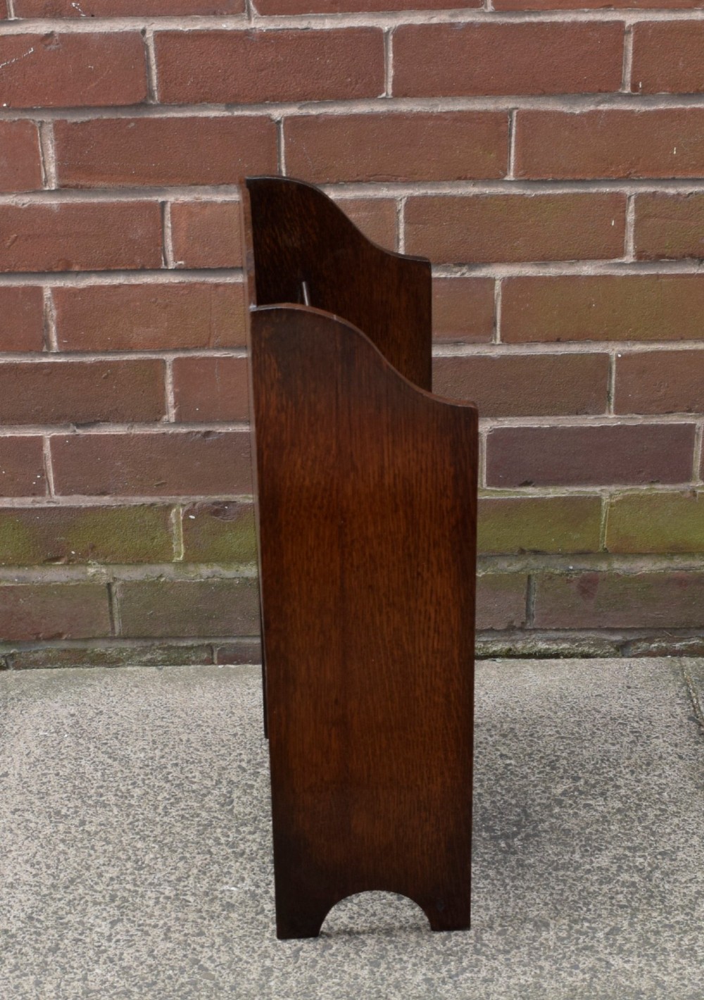 A dark oak Arts and Crafts freestanding magazine rack featuring a gently arched crest rail and three tiered open compartments. View XI