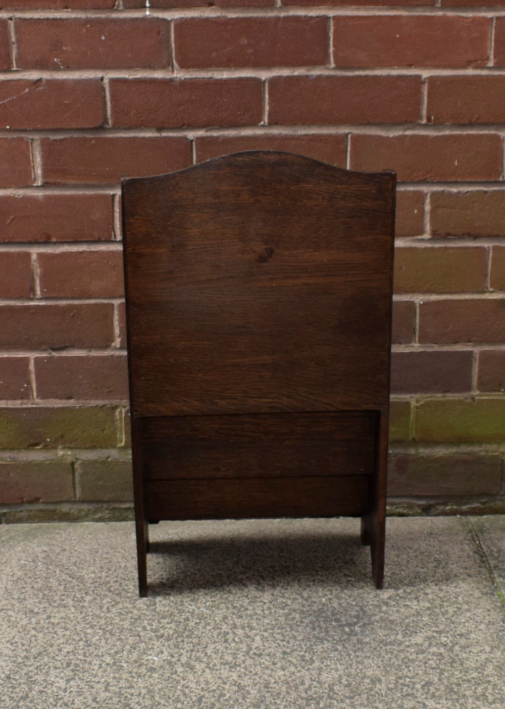 A dark oak Arts and Crafts freestanding magazine rack featuring a gently arched crest rail and three tiered open compartments. View XII