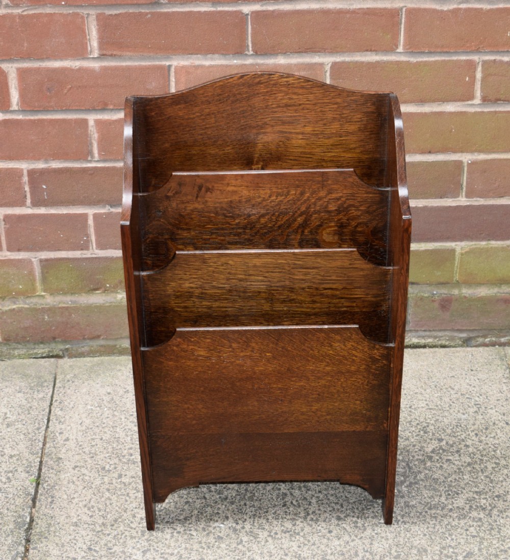 A dark oak Arts and Crafts freestanding magazine rack featuring a gently arched crest rail and three tiered open compartments. View XIII