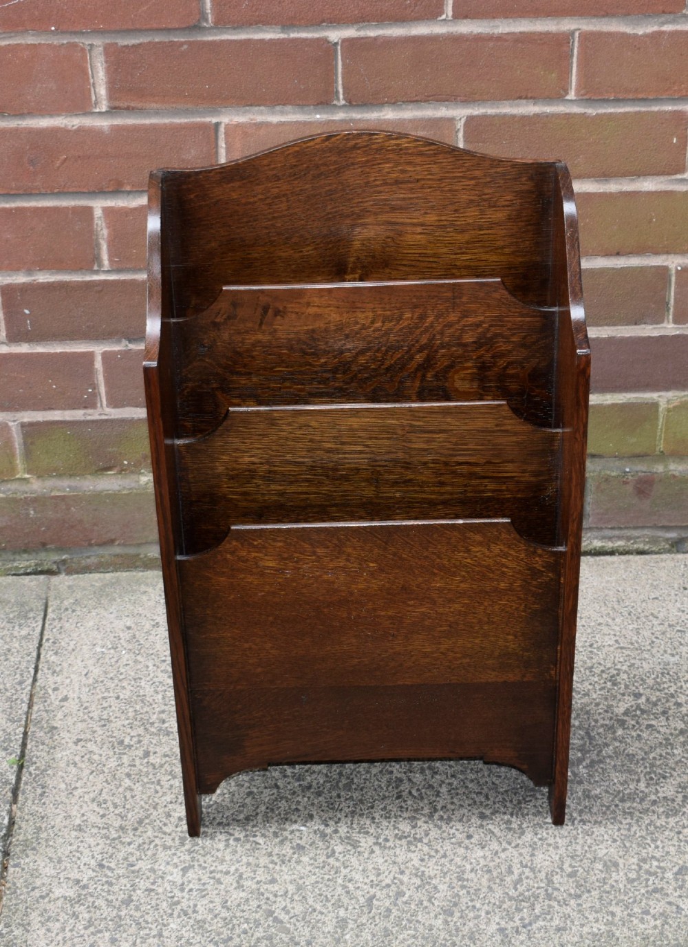 A dark oak Arts and Crafts freestanding magazine rack featuring a gently arched crest rail and three tiered open compartments. View XIV