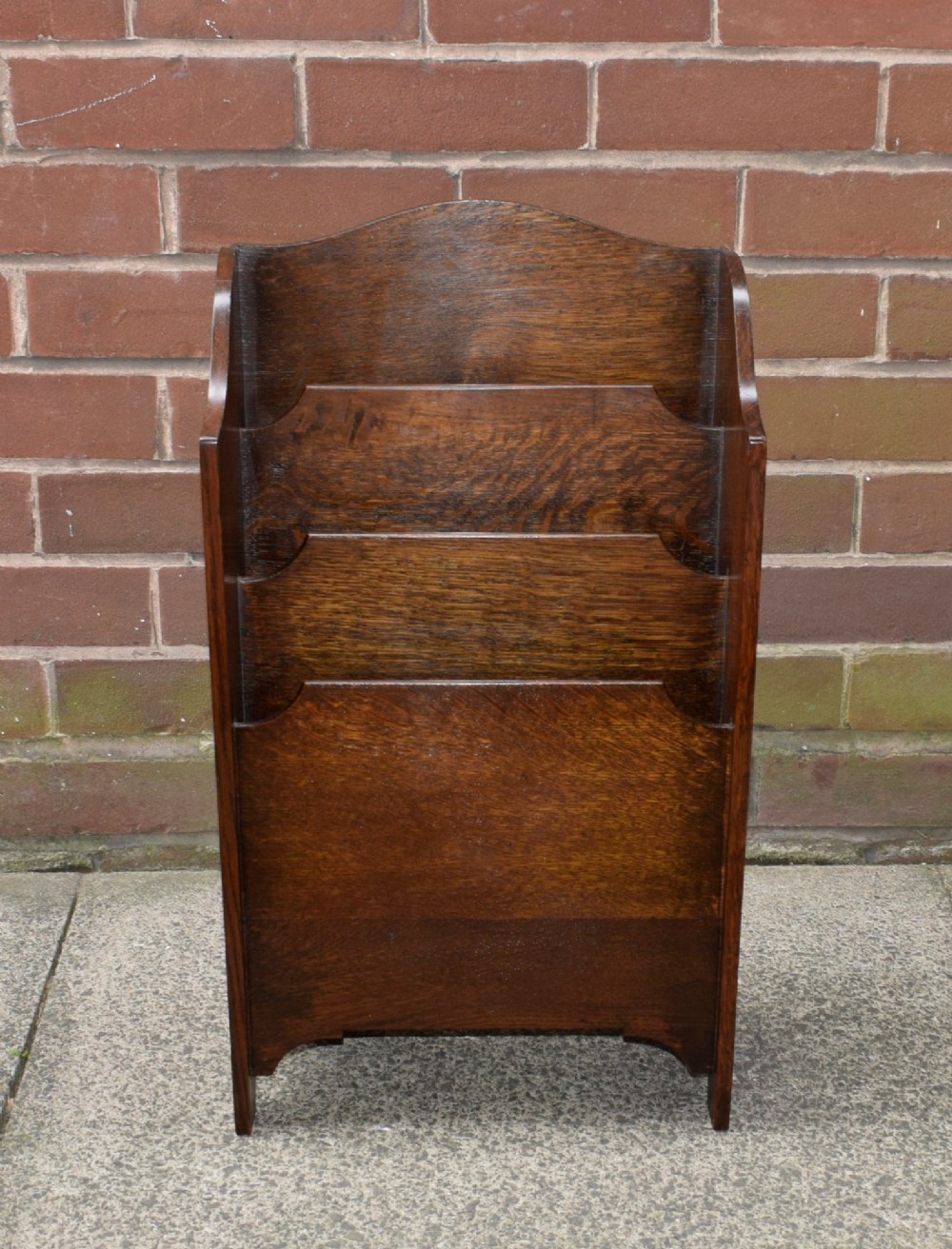 A dark oak Arts and Crafts freestanding magazine rack featuring a gently arched crest rail and three tiered open compartments. View XV