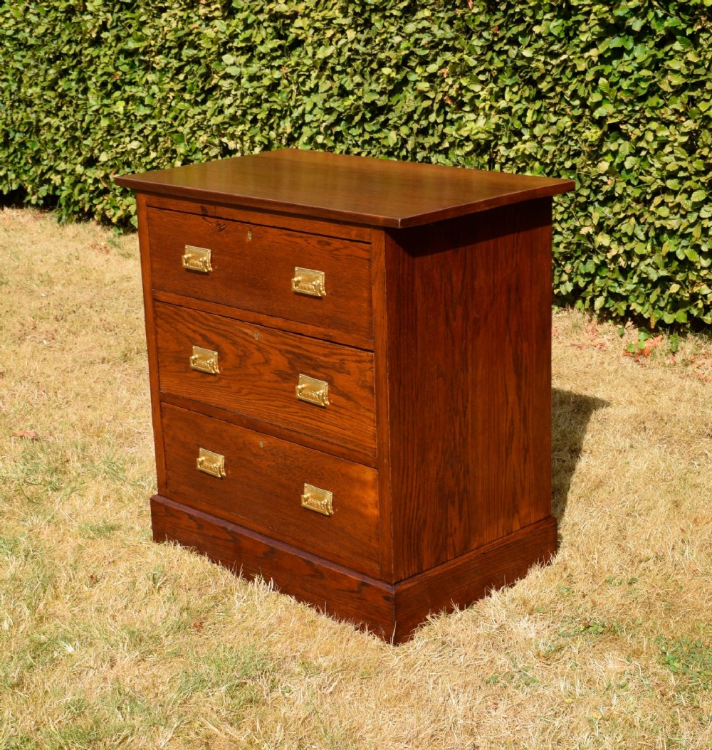 A medium-toned oak chest of drawers featuring three drawers with rectangular brass handles resting on a plinth base.