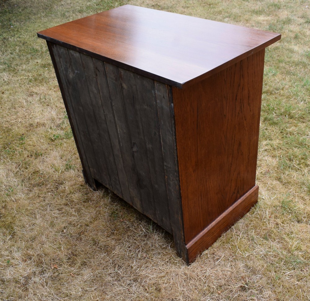 A medium-toned oak chest of drawers featuring three drawers with rectangular brass handles resting on a plinth base. View XI