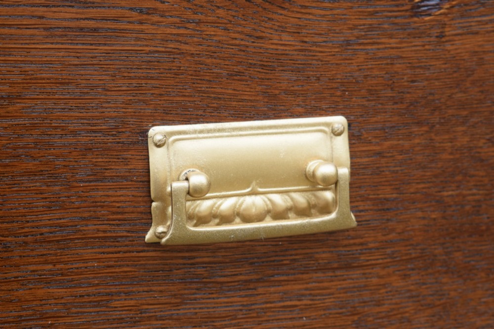 A medium-toned oak chest of drawers featuring three drawers with rectangular brass handles resting on a plinth base. View XII