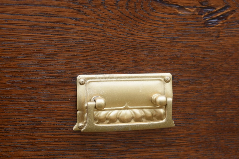 A medium-toned oak chest of drawers featuring three drawers with rectangular brass handles resting on a plinth base. View XIII