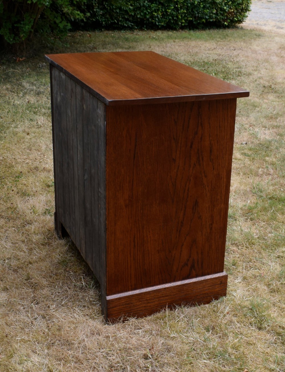 A medium-toned oak chest of drawers featuring three drawers with rectangular brass handles resting on a plinth base. View XIV
