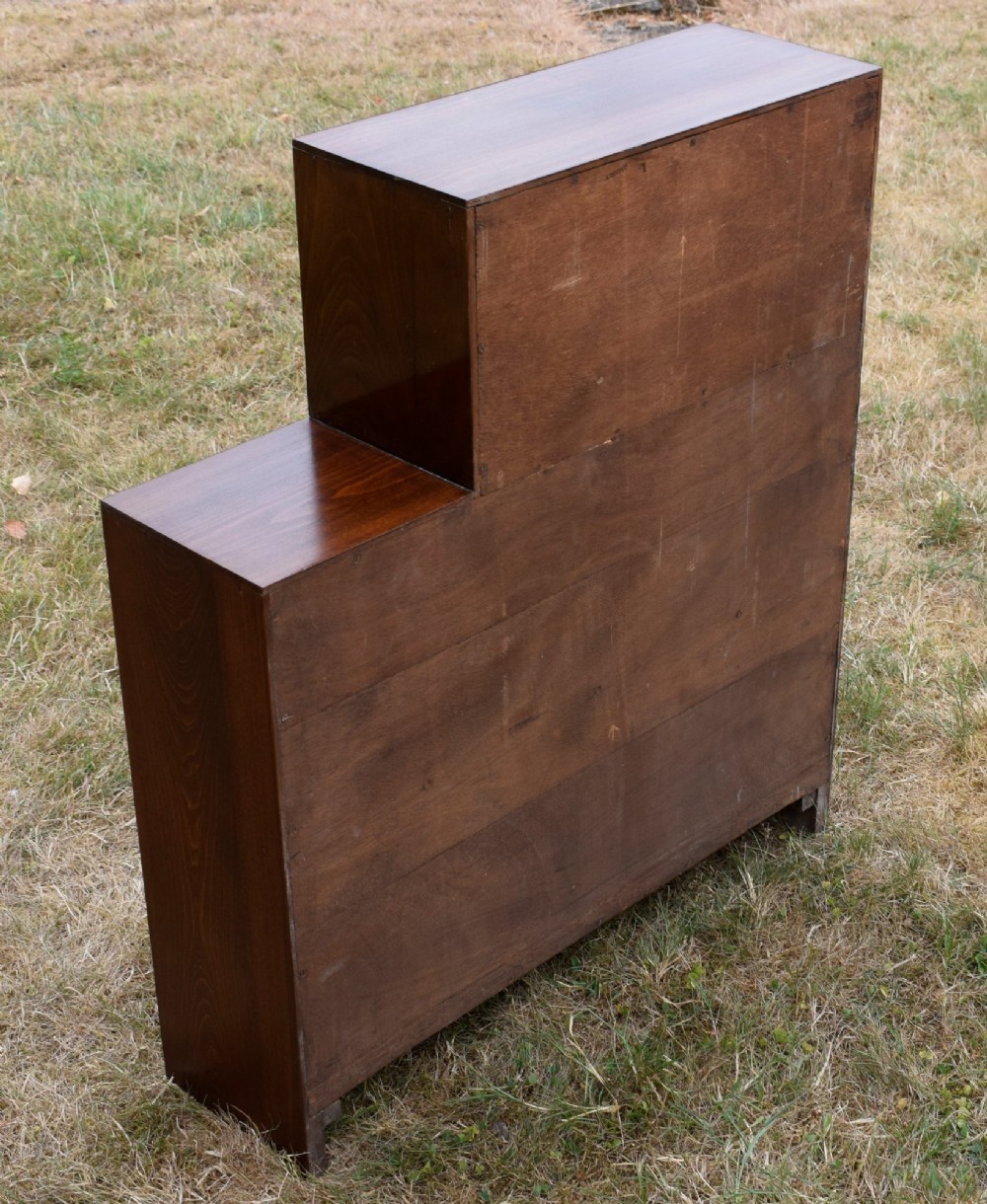 A dark brown wooden Art Deco bookcase featuring an asymmetrical stepped design with three open shelves. View VI