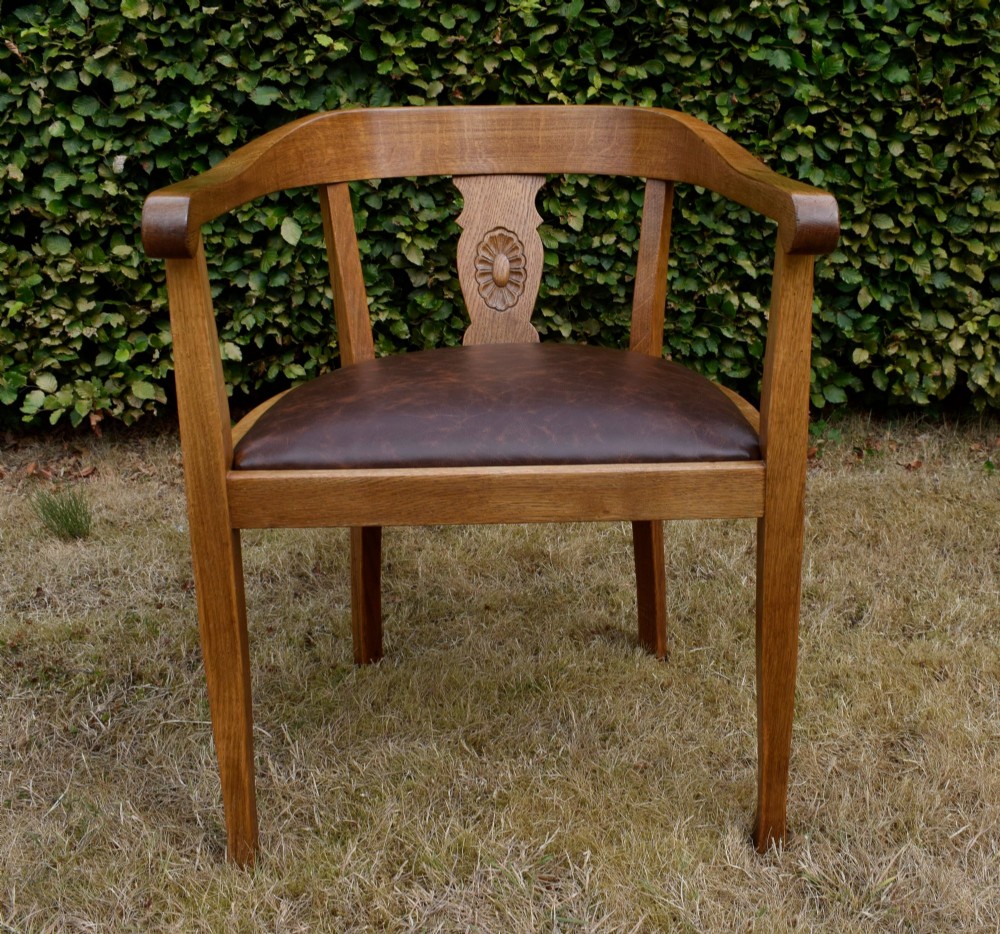 An early 20th-century oak desk chair featuring a curved horseshoe backrest, a carved central splat, and a dark brown upholstered seat pad.
