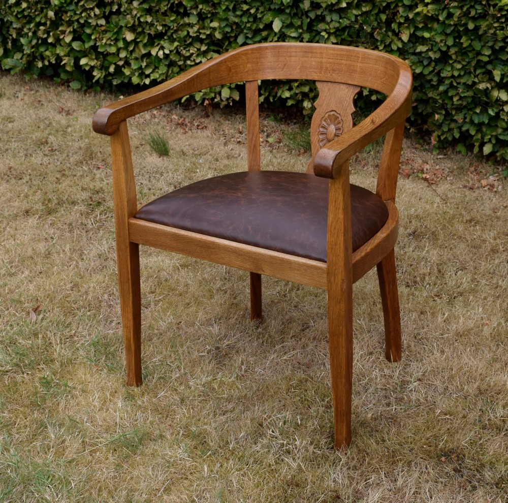 An early 20th-century oak desk chair featuring a curved horseshoe backrest, a carved central splat, and a dark brown upholstered seat pad. View III