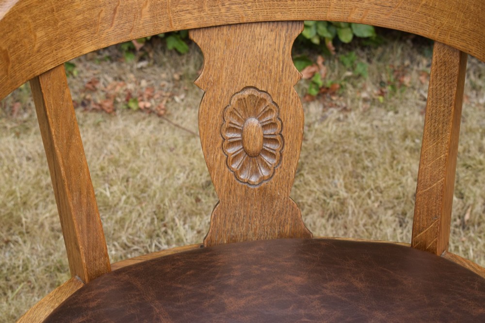 An early 20th-century oak desk chair featuring a curved horseshoe backrest, a carved central splat, and a dark brown upholstered seat pad. View V