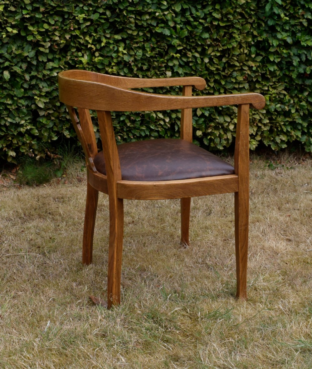 An early 20th-century oak desk chair featuring a curved horseshoe backrest, a carved central splat, and a dark brown upholstered seat pad. View VII