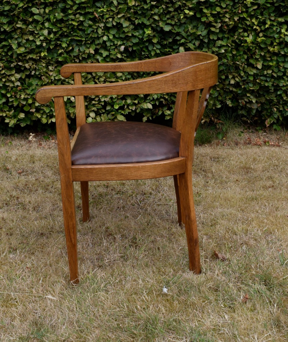 An early 20th-century oak desk chair featuring a curved horseshoe backrest, a carved central splat, and a dark brown upholstered seat pad. View VIII