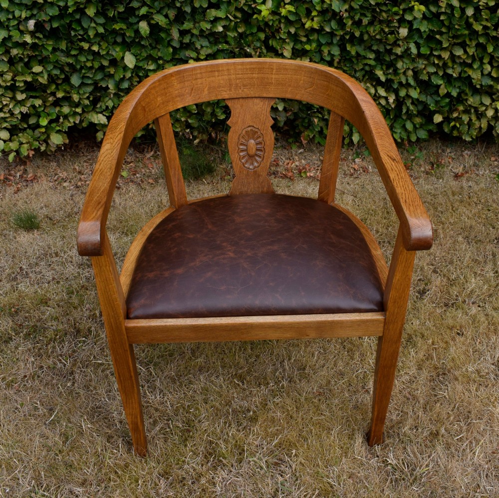 An early 20th-century oak desk chair featuring a curved horseshoe backrest, a carved central splat, and a dark brown upholstered seat pad. View IX