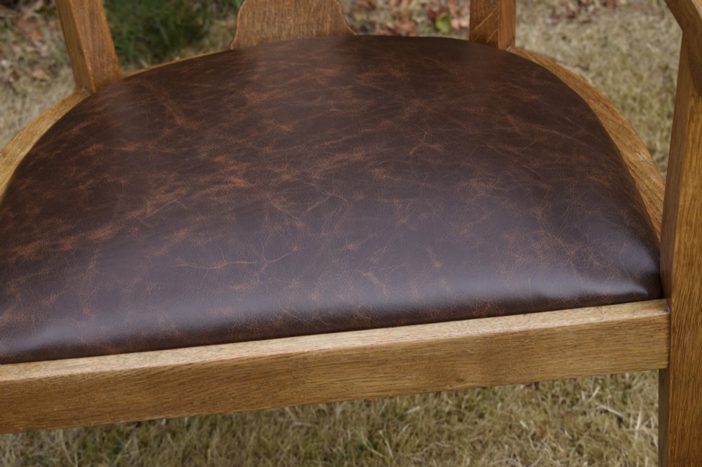 An early 20th-century oak desk chair featuring a curved horseshoe backrest, a carved central splat, and a dark brown upholstered seat pad. View X