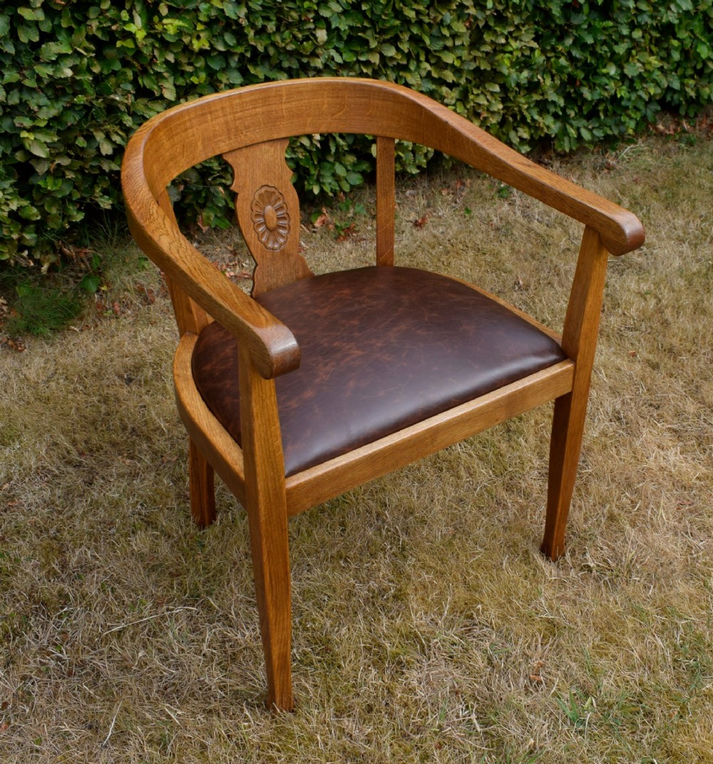 An early 20th-century oak desk chair featuring a curved horseshoe backrest, a carved central splat, and a dark brown upholstered seat pad. View XII
